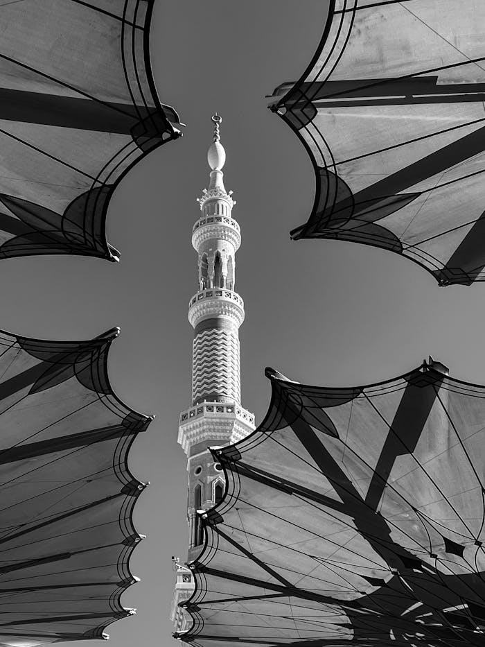 A captivating black and white photograph of a minaret framed by umbrellas in Medina, Saudi Arabia.