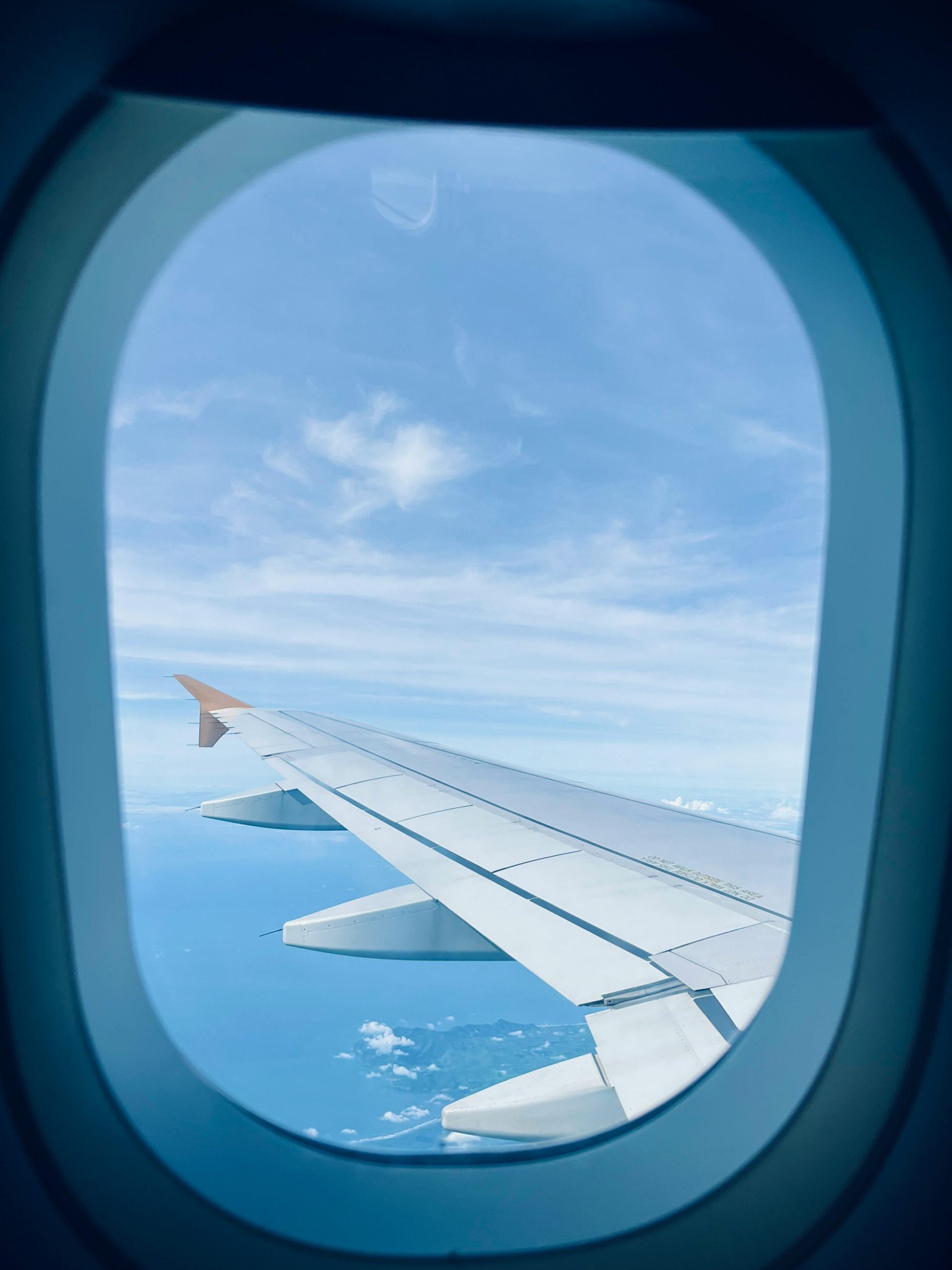 A scenic aerial view of an airplane wing through an aircraft window, showcasing the clear blue sky.